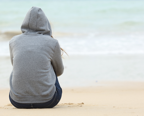 Woman in hoodie sitting on the beach on a winter morning