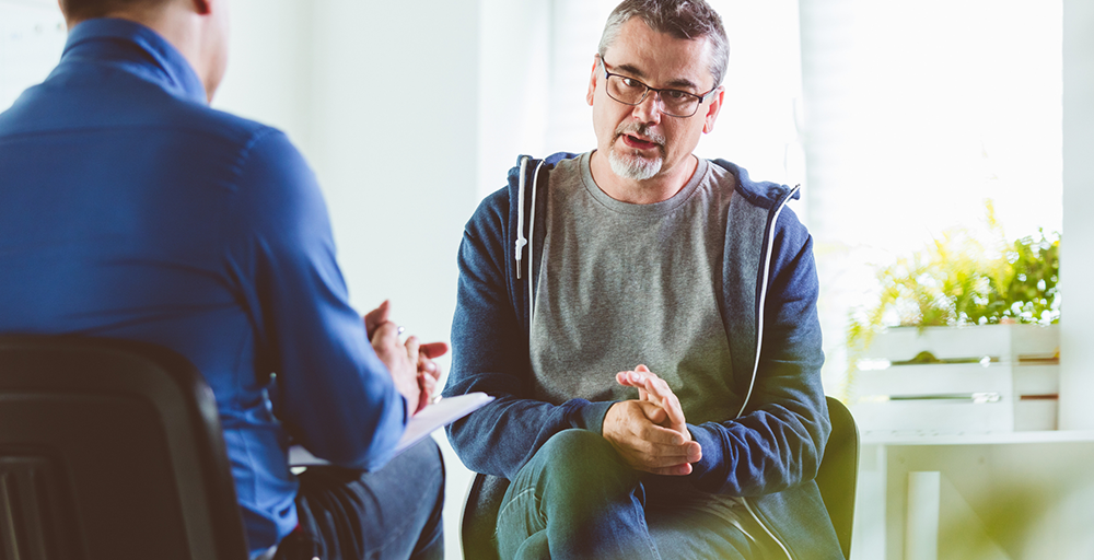 Older man talking to mental health psychologist in brightly lit room