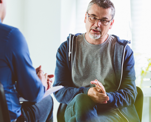 Older man talking to mental health psychologist in brightly lit room