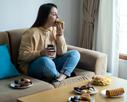 Woman eating sugary food on sofa eating disorders concept image